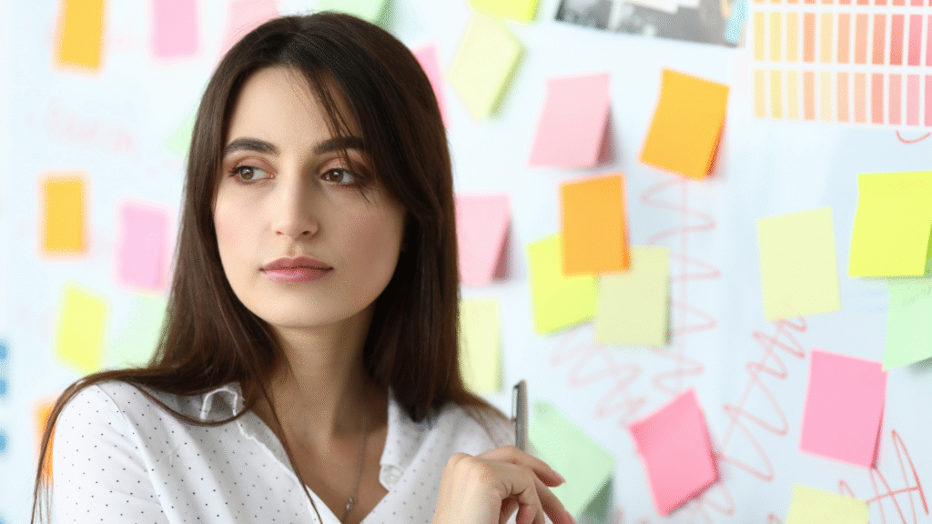 Uma mulher olhando pensativa com um quadro cheio de notas atrás dela. Para demonstrar como conciliar trabalho CLT com a criação de conteúdo